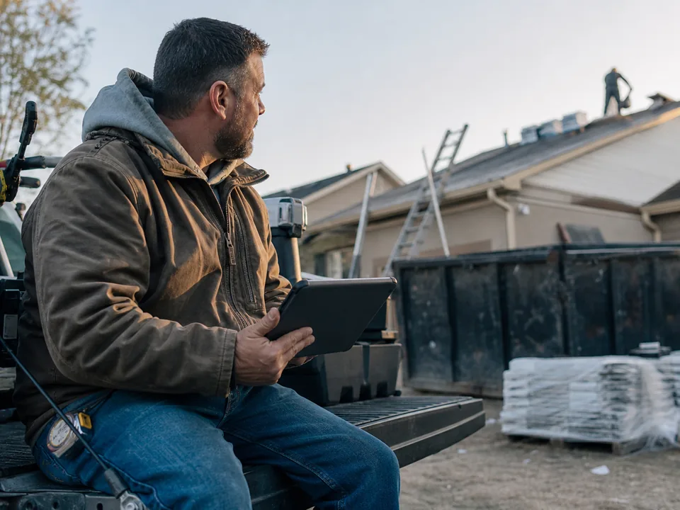 Roofing contractor reviewing leads and ad results on a tablet on the tailgate of his truck at a job site